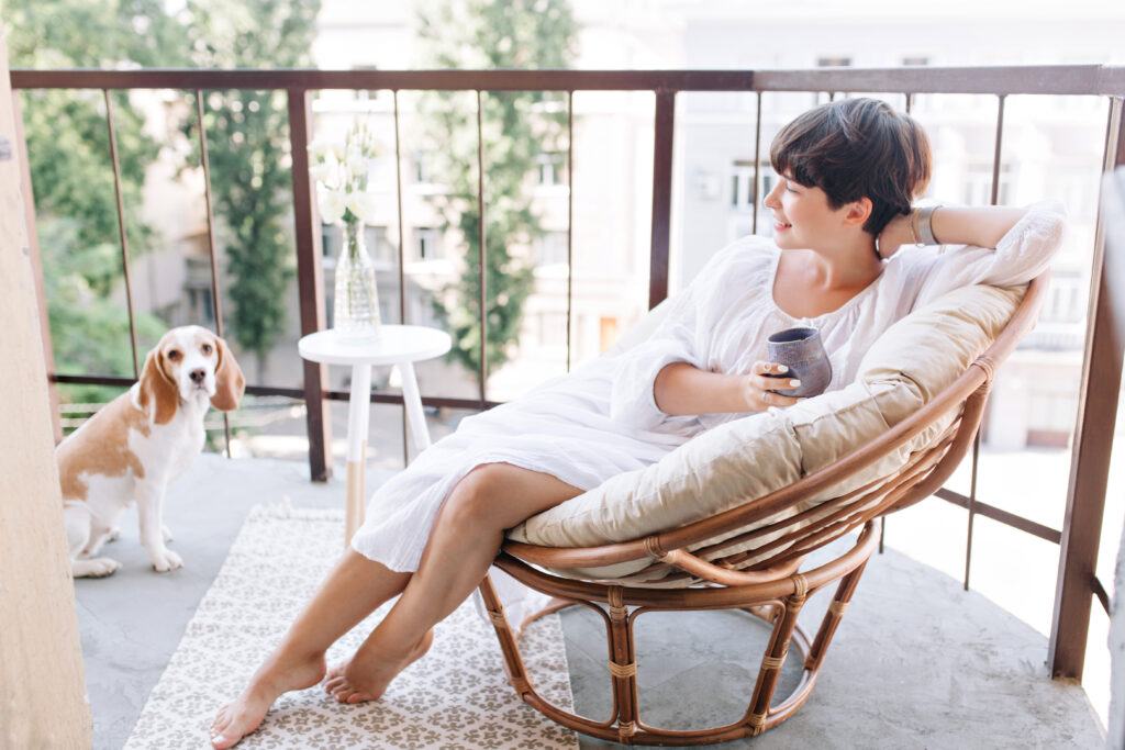 relaxed barefooted girl white dress sitting chair balcony holding cup tea