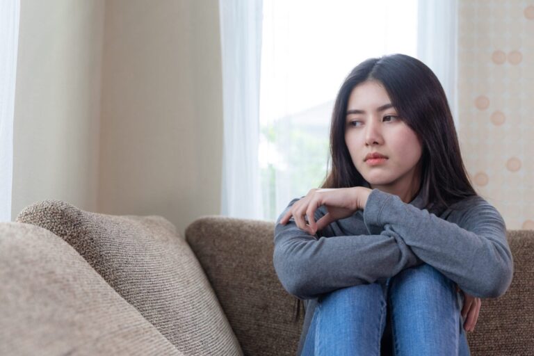 Unhappy asian pretty young woman siting alone couch with feeling sadness scaled