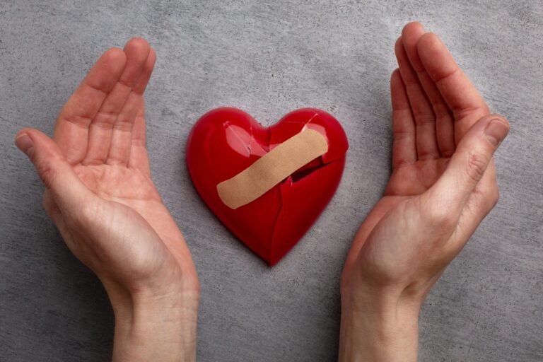 Broken plastic red heart grey background top view scaled